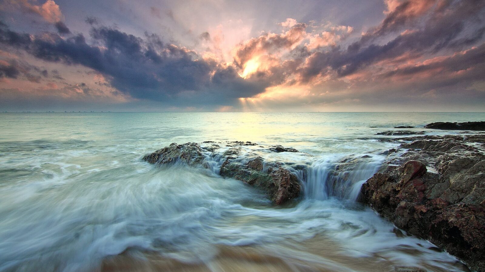 A sunset at a rocky beach. The sunlight shines through the clouds.